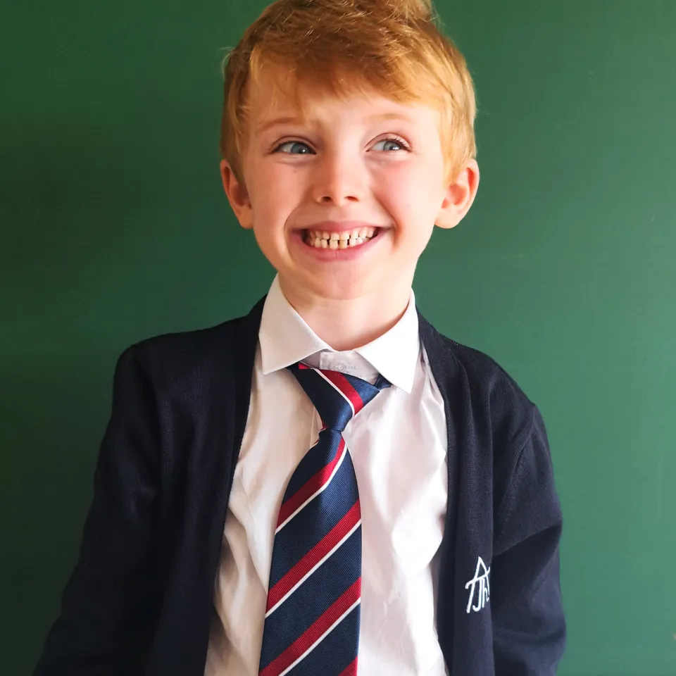 Frecher junger Bursche in Schuluniform mit breitem Lachen und roten Haaren vor einer Schultafel stehend
