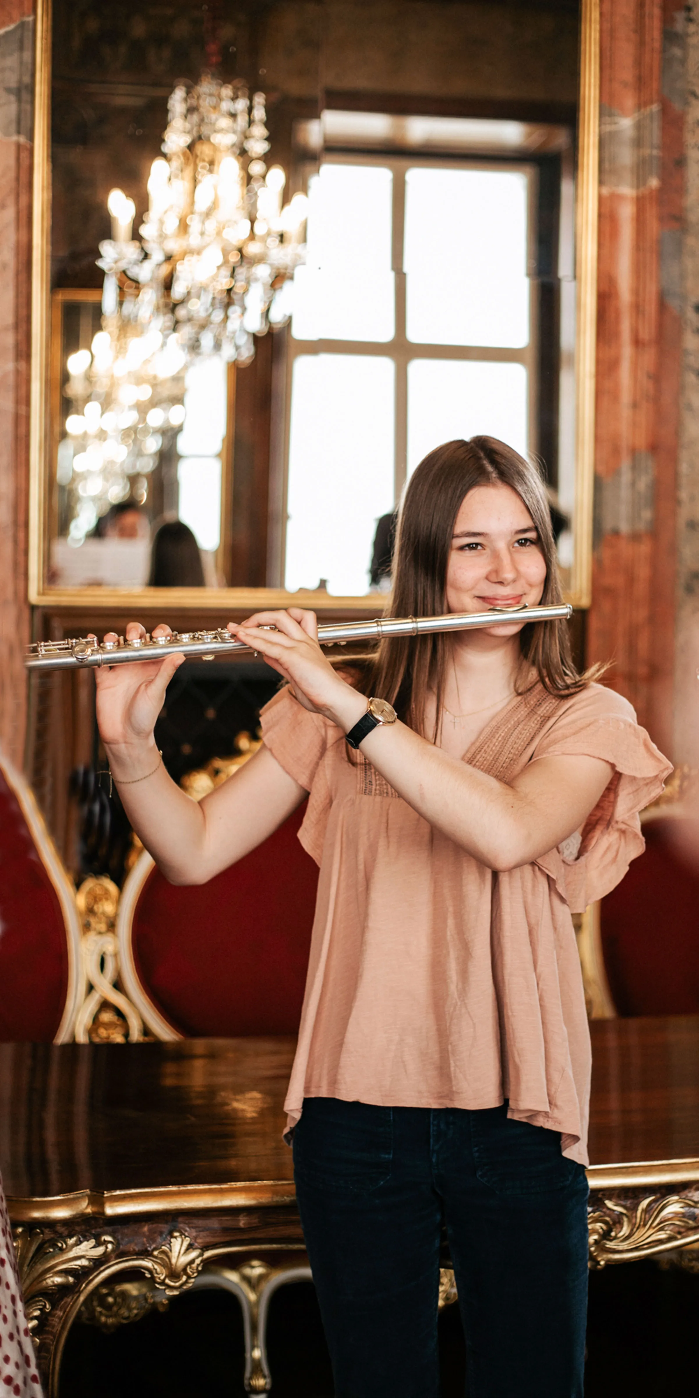 Junges Mädchen mit brünetten langen Haaren und hellerbrauner Bluse in historischem Ambiente Querflöte spielend