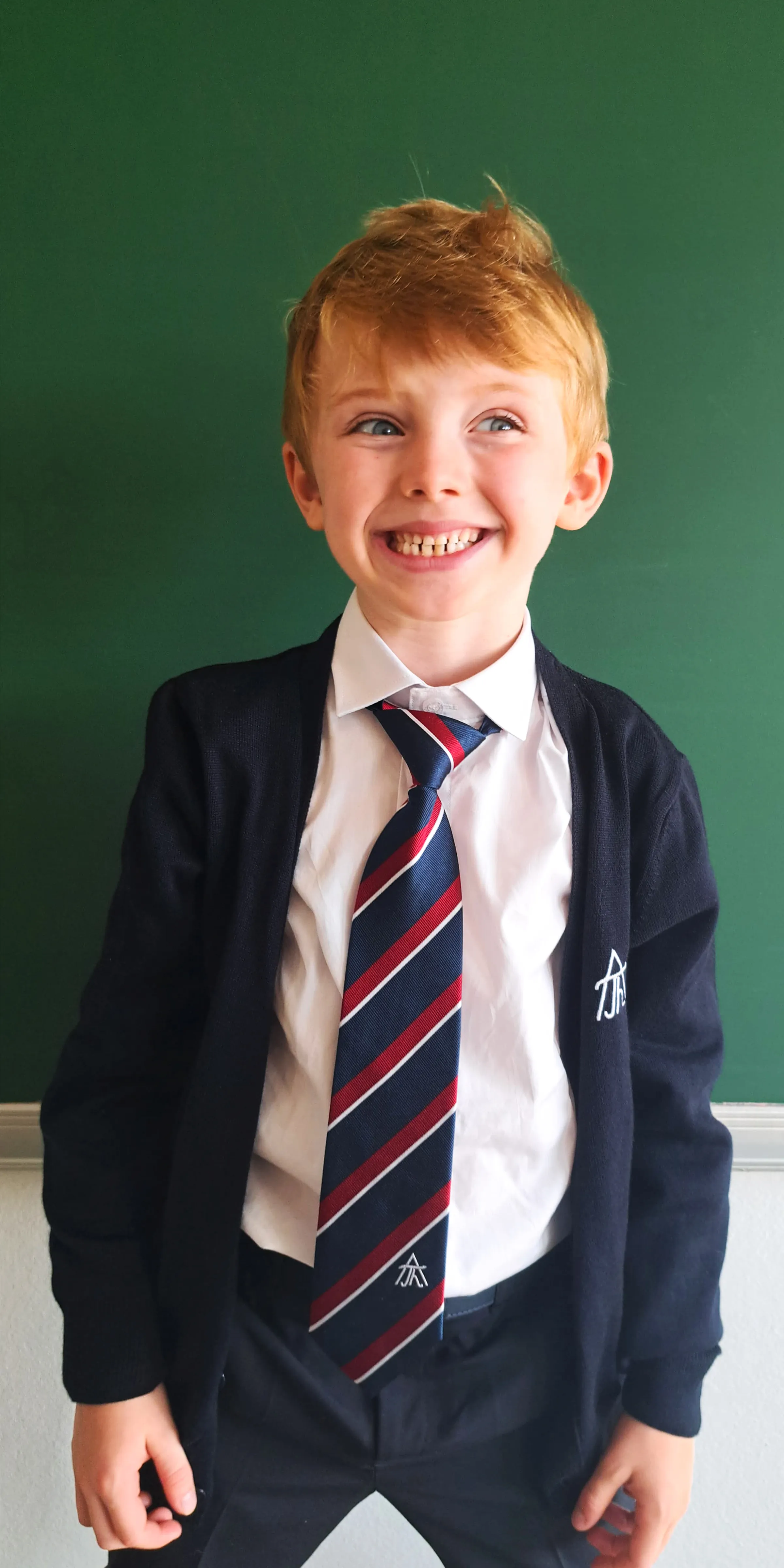 breit grinsender junger Bursche mit roten Haaren in schuluniform vor einer Schultafel sehend