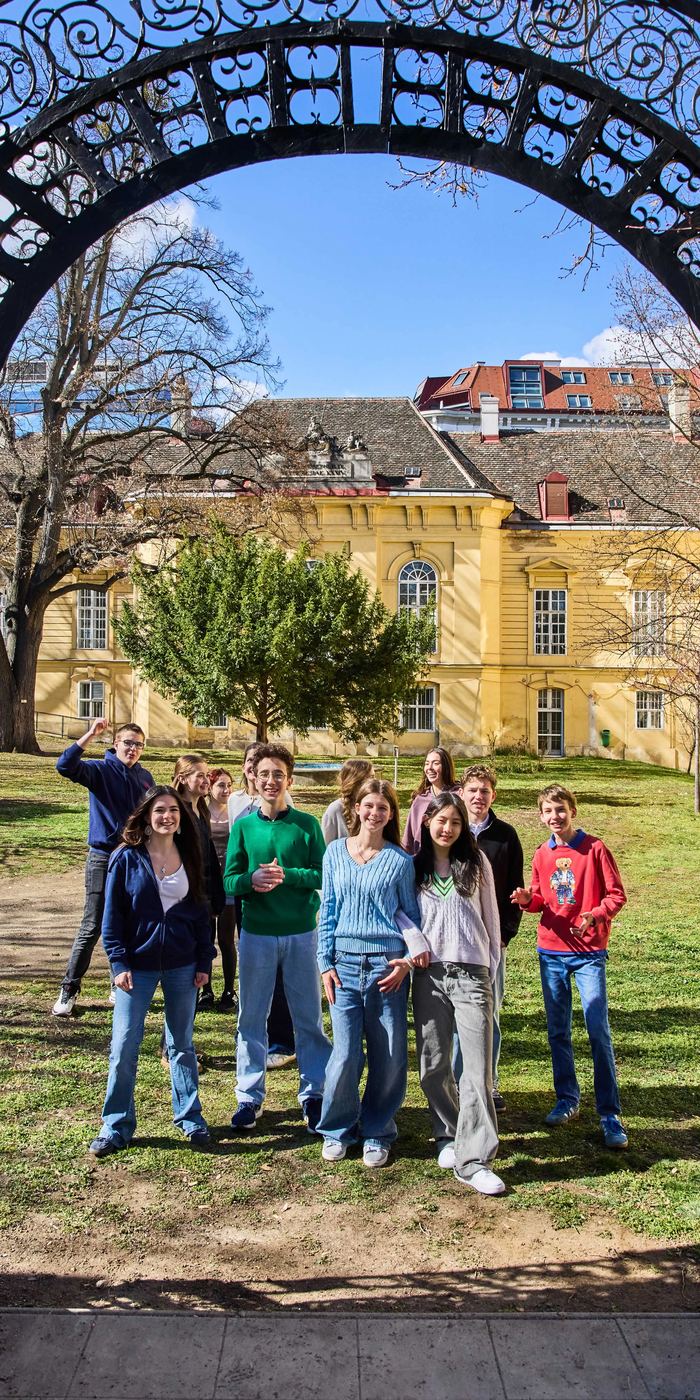 Gruppe von Burschen und Mädchen in einem wunderschönen Torbogen stehend und in die Kamera lachend mit einem barocken Gebäude im Hintergrund bei strahlend blauem Himmel