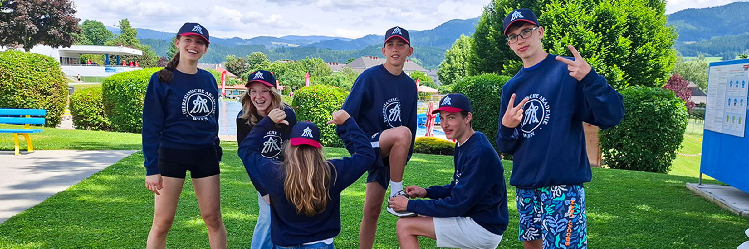 Gruppe von Jugendlichen in Shorts und einheitlichem dunkelblauem Sweater teilweise und Caps mit Peace Zeichen in die Kamera lachend