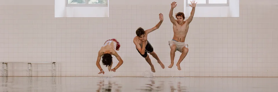 Drei Burschen in ein Hallenschwimmbad springend
