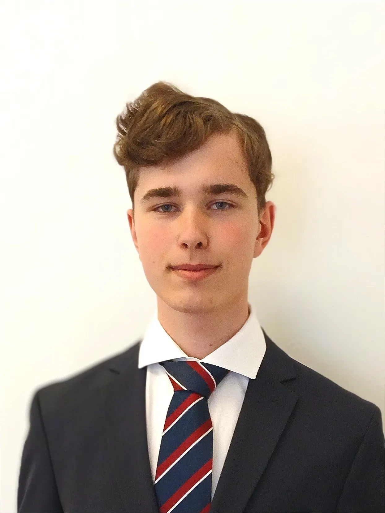 Junge Mann in Anzug und Krawatte vor einem neutralen Hintergrund stehend mit modernen lockigen Haaren