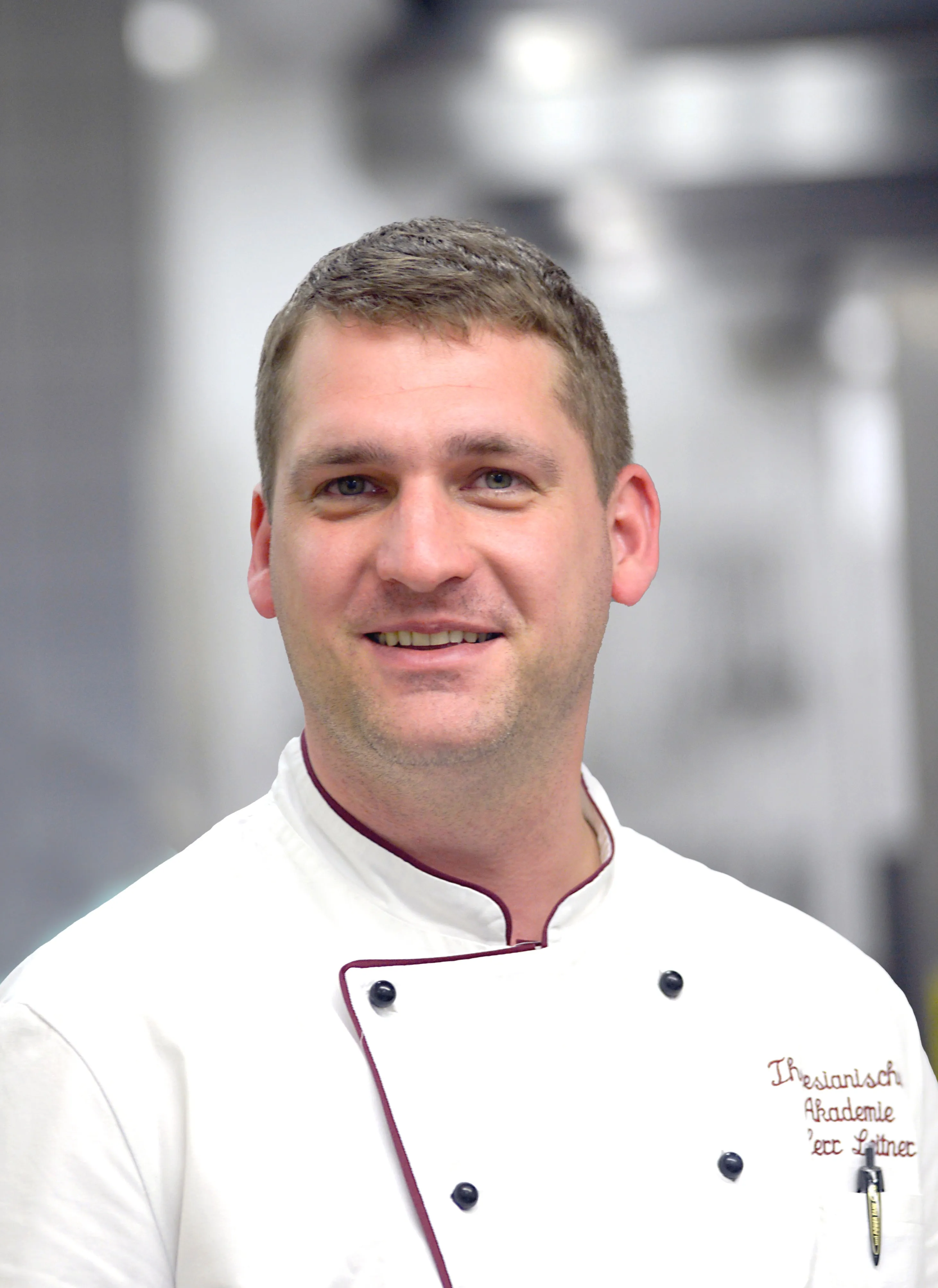 Portraitfoto eines Mannes mit kurzen brünetten Haaren und freundlichem Lachen in Küchenuniform