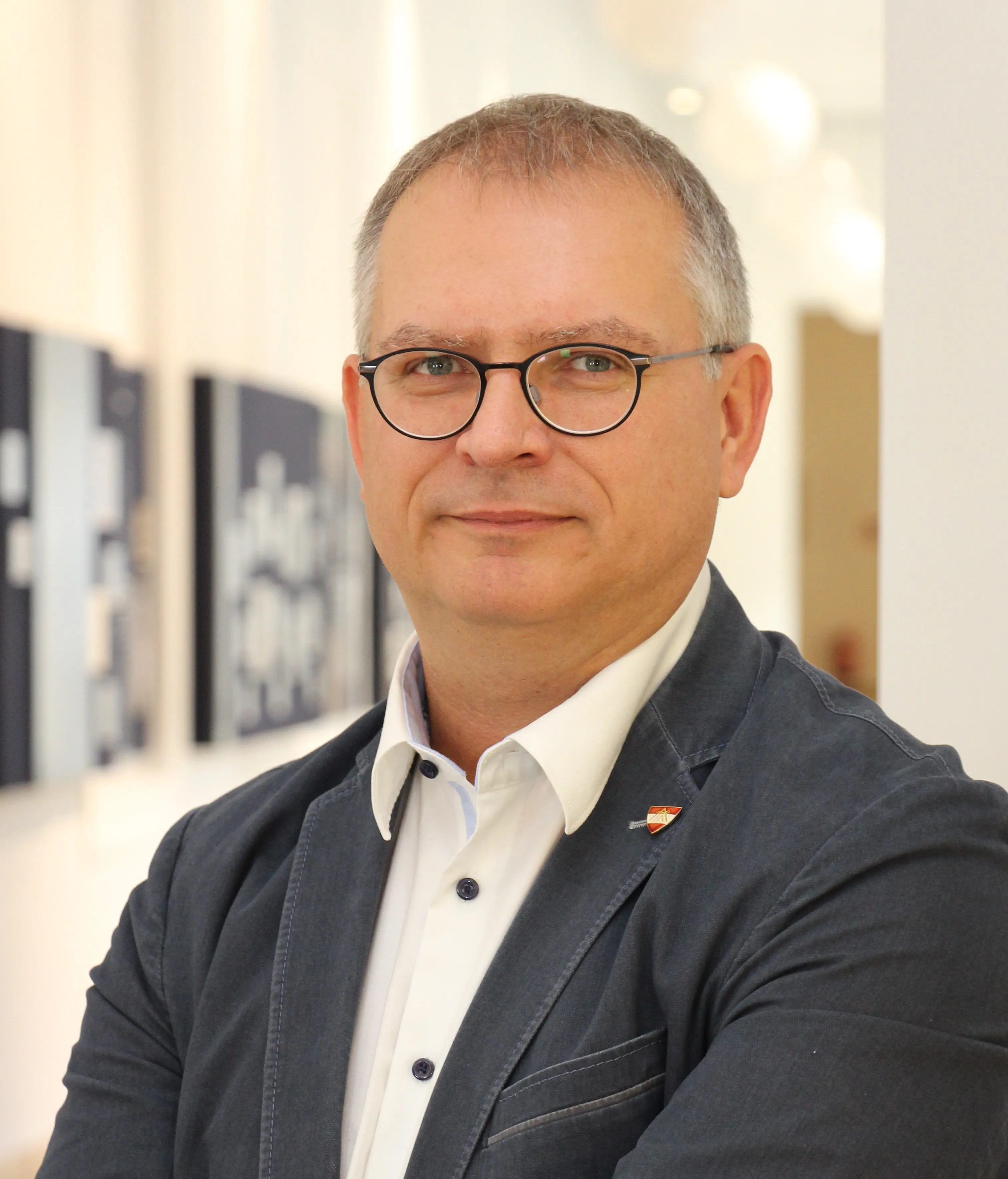 Ein Mann mit Brille, einem weißen Hemd und einer dunklen Jacke.