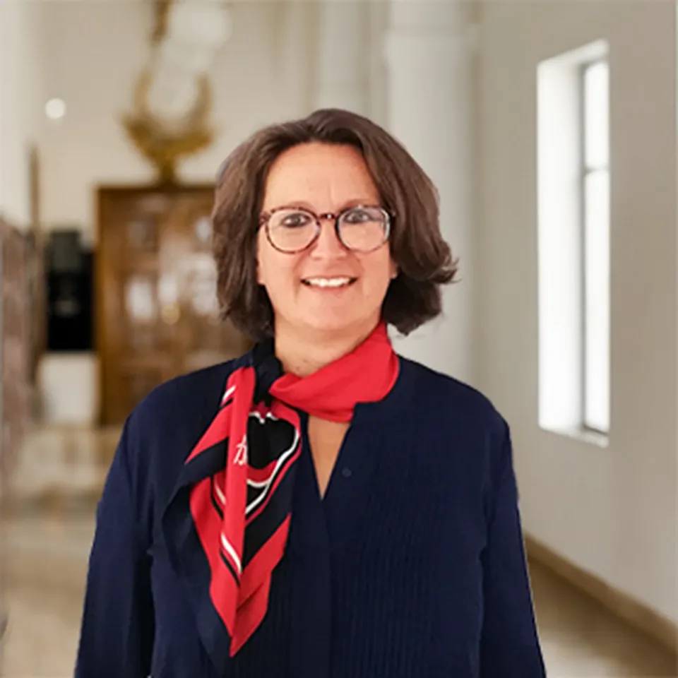 Lächelnde Frau mit kurzem braunen Haar und Brille, die das rot-blaue Theresianum Tuch trägt.