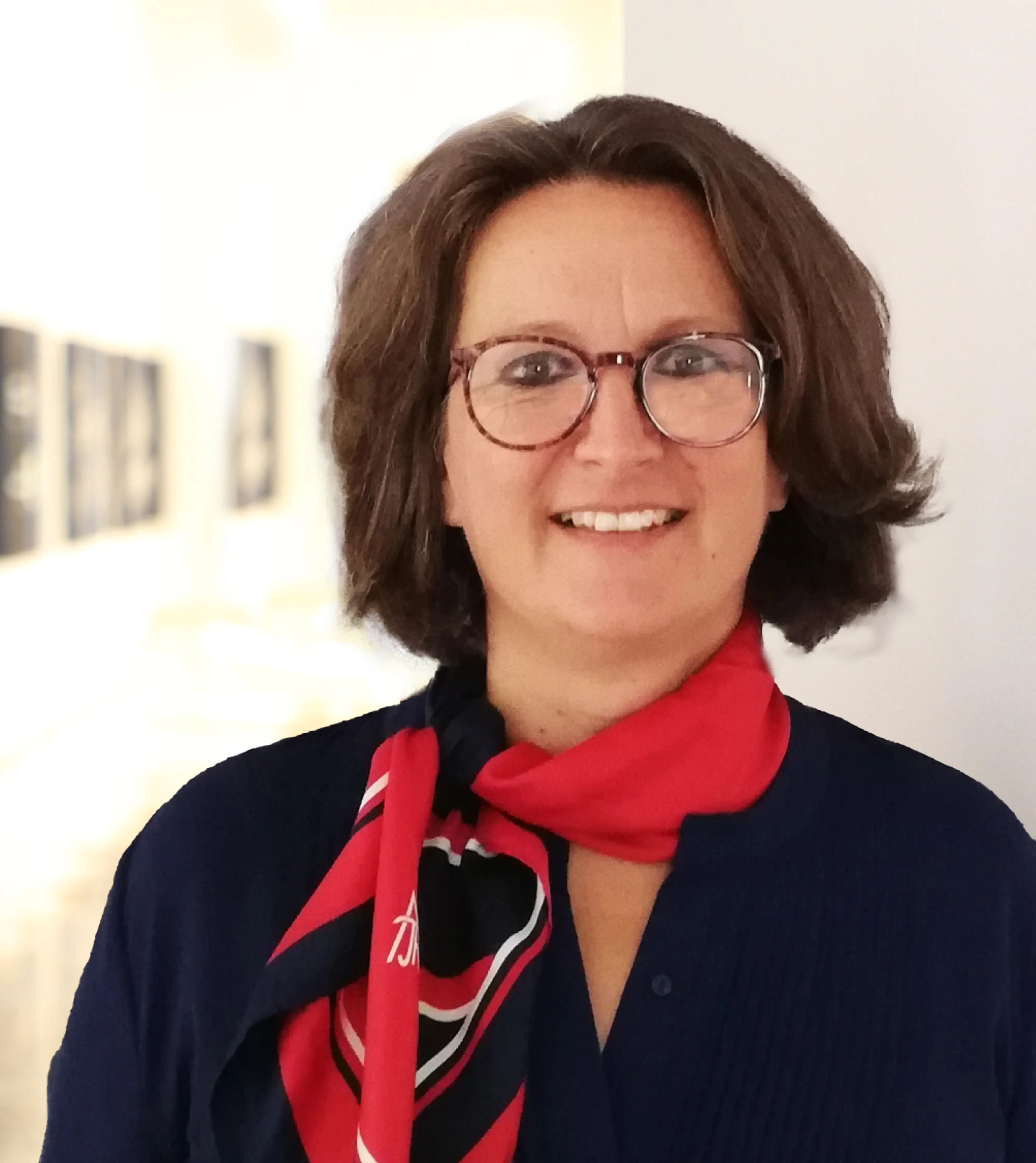 Lächelnde Frau mit kurzem braunen Haar und Brille, die das rot-blaue Theresianum Tuch trägt.