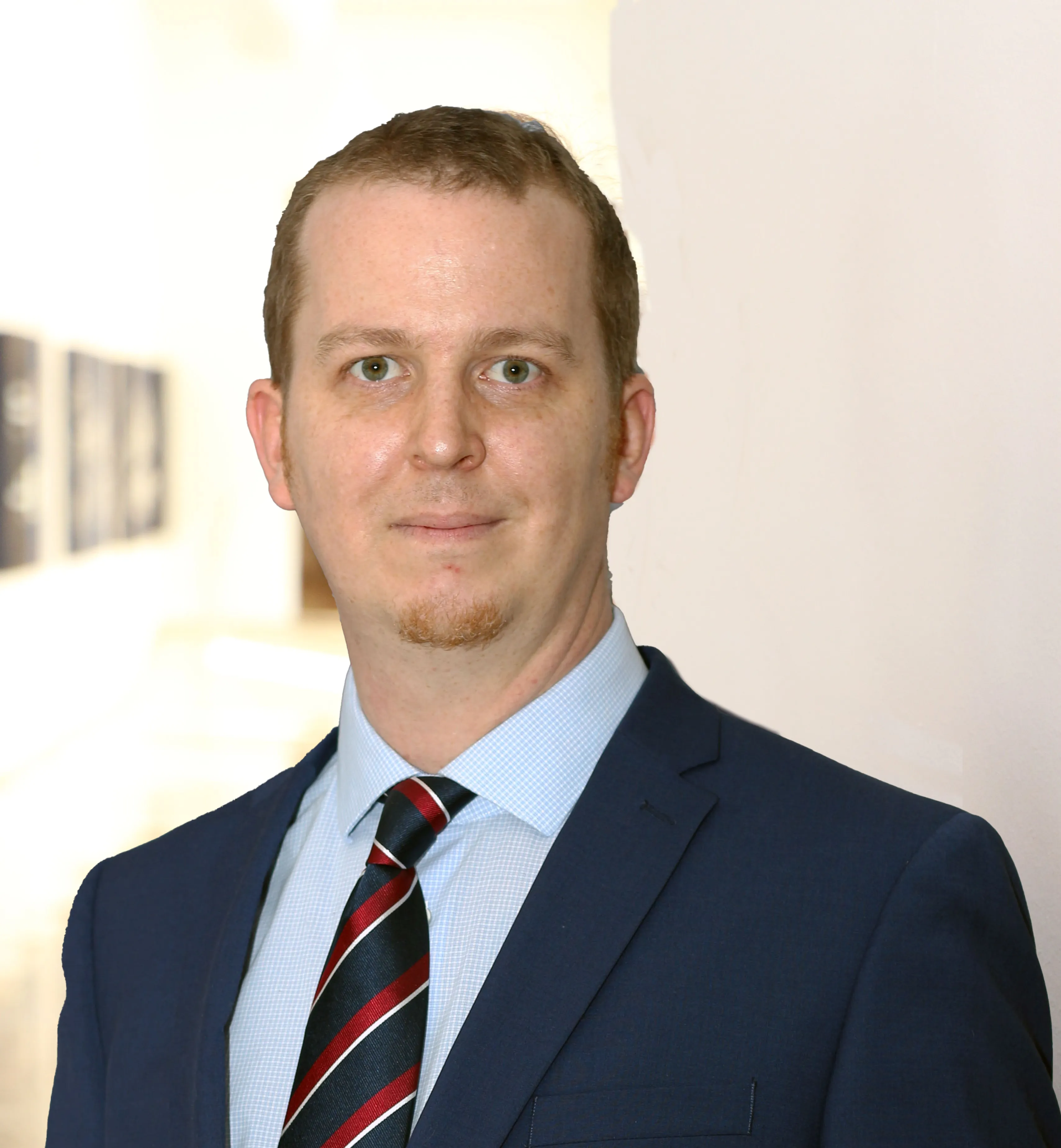 Mann mit kurzem Haar im dunkelblauen Anzug und rot-blauer Krawatte.