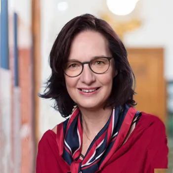 Portrait einer Frau mit Brille und dunklen mittellangen Haaren einem roten Oberteil und einem rot-blau-weißem Halstuch