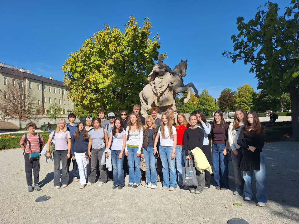 A group of young people posing in front of a horse statue in a park with trees, under a clear blue sky.