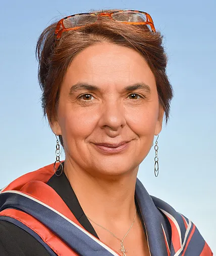 portraitfoto einer frau mittleren alters mit roter Lesebrille im kurzen brünettenhaar steckend und langen ohrringen, kreuz anhänger um den hals und rot blauen Halstuch