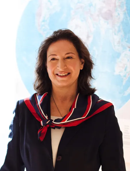 sympathisch lachende Frau in elegantem Business Outfit und rot blauem Halstuch und mittellangemen brünetten Haar vor einer Weltkarte