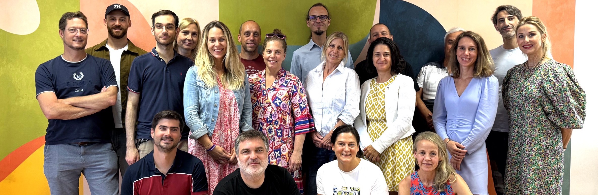 Gruppe von erwachsenen Menschen vor einer bunten Wand stehend und hockend.
