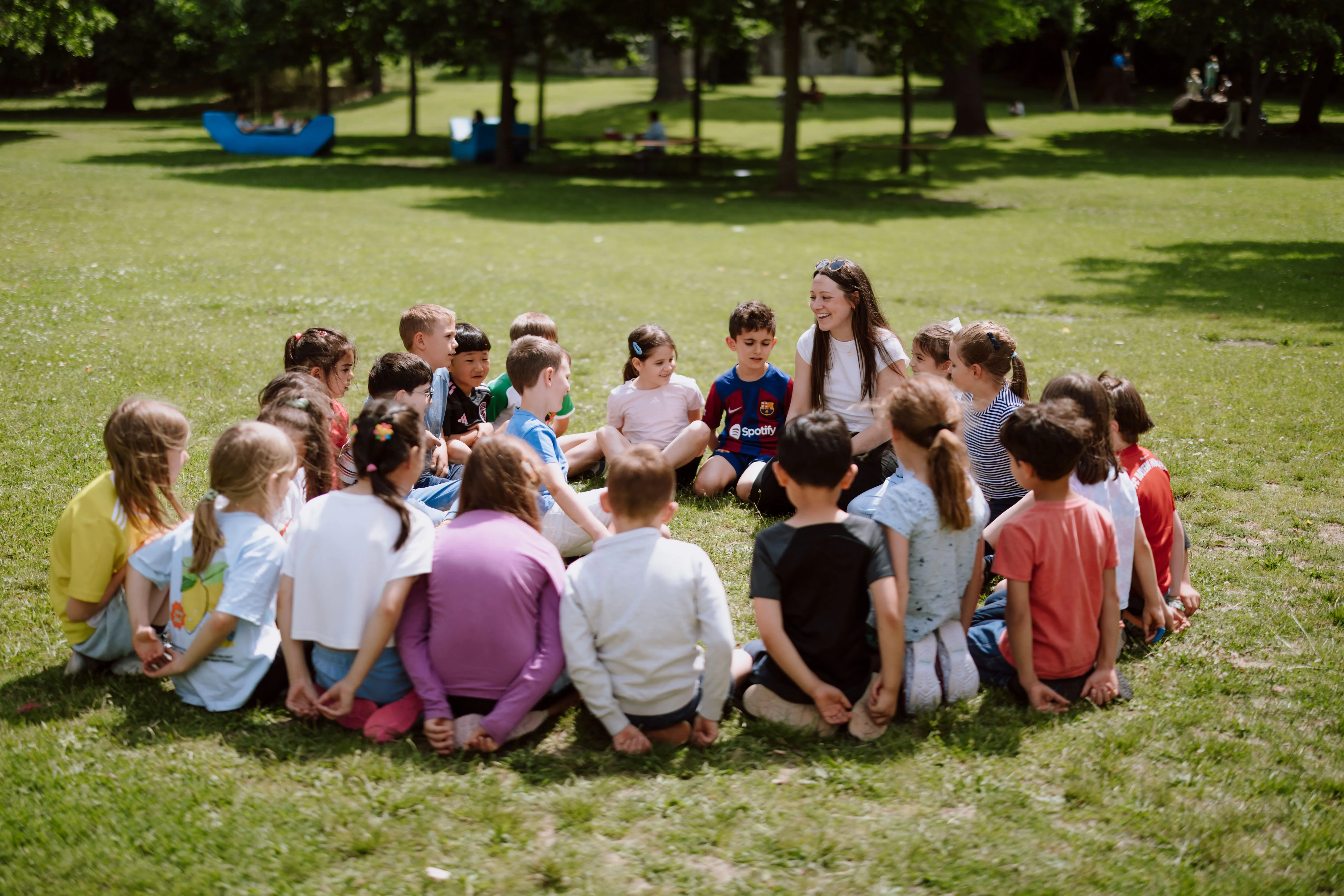 Kindergruppe im Sitzkreis auf einer sonnigen Wiese sitzend