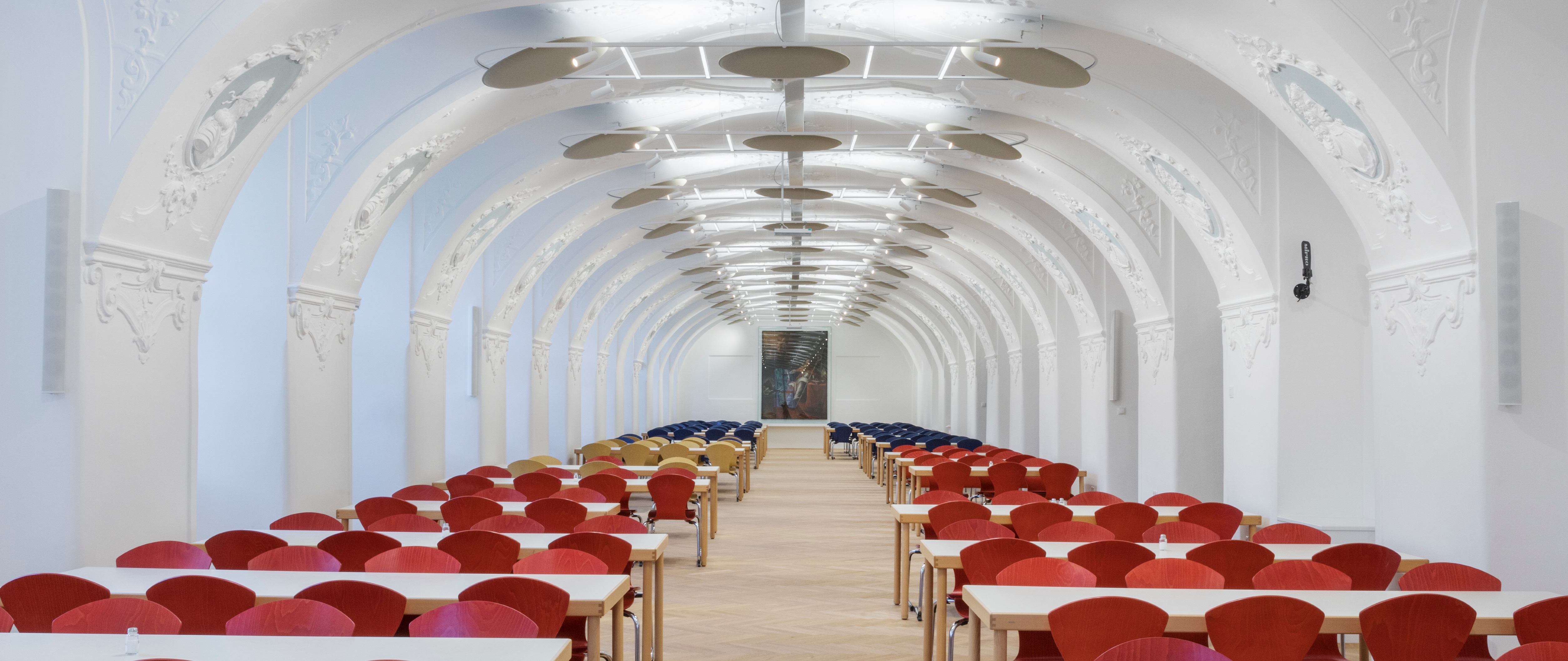 Speisesaal in historischem Gewölbe mit Stuck und Tischen mit roten Stühlen