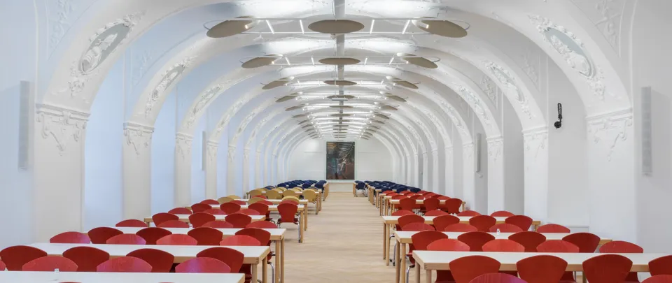 Speisesaal in historischem Gewölbe mit Stuck und Tischen mit roten Stühlen