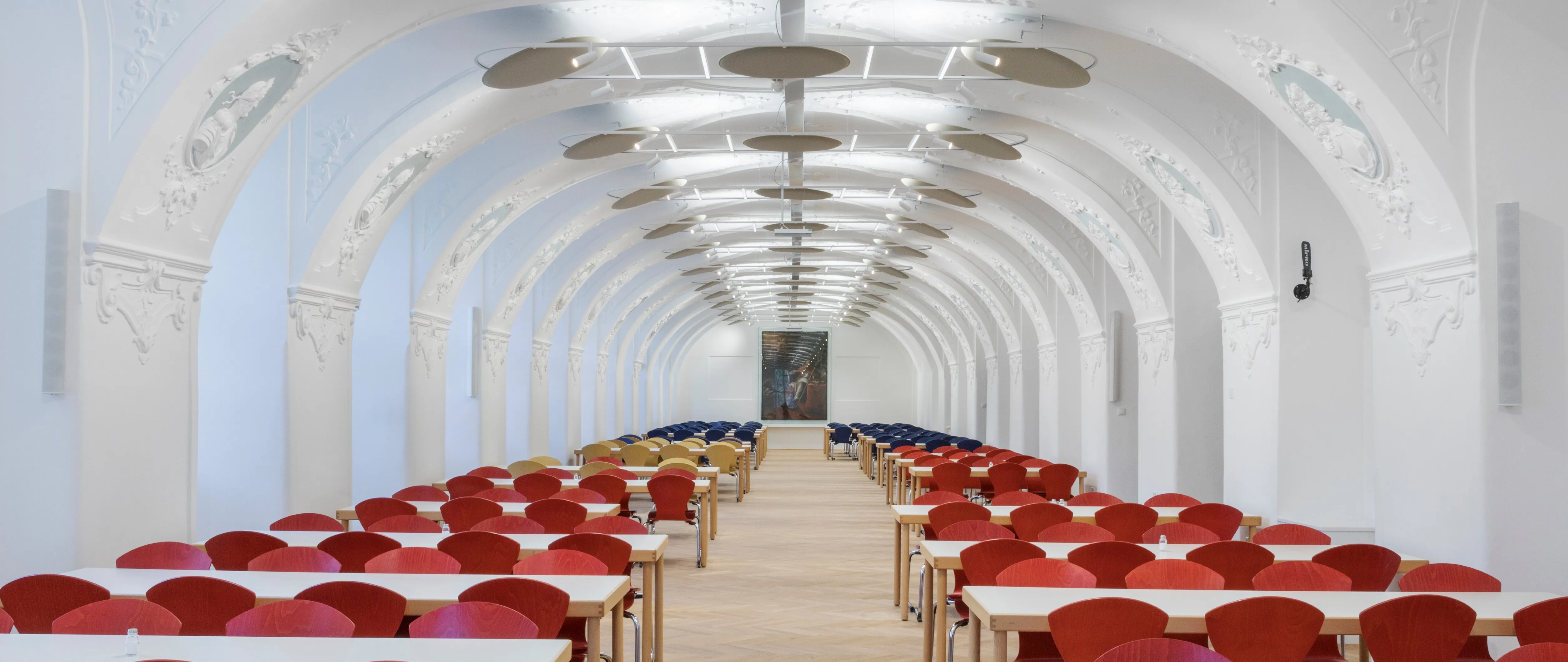 Speisesaal in historischem Gewölbe mit Stuck und Tischen mit roten Stühlen