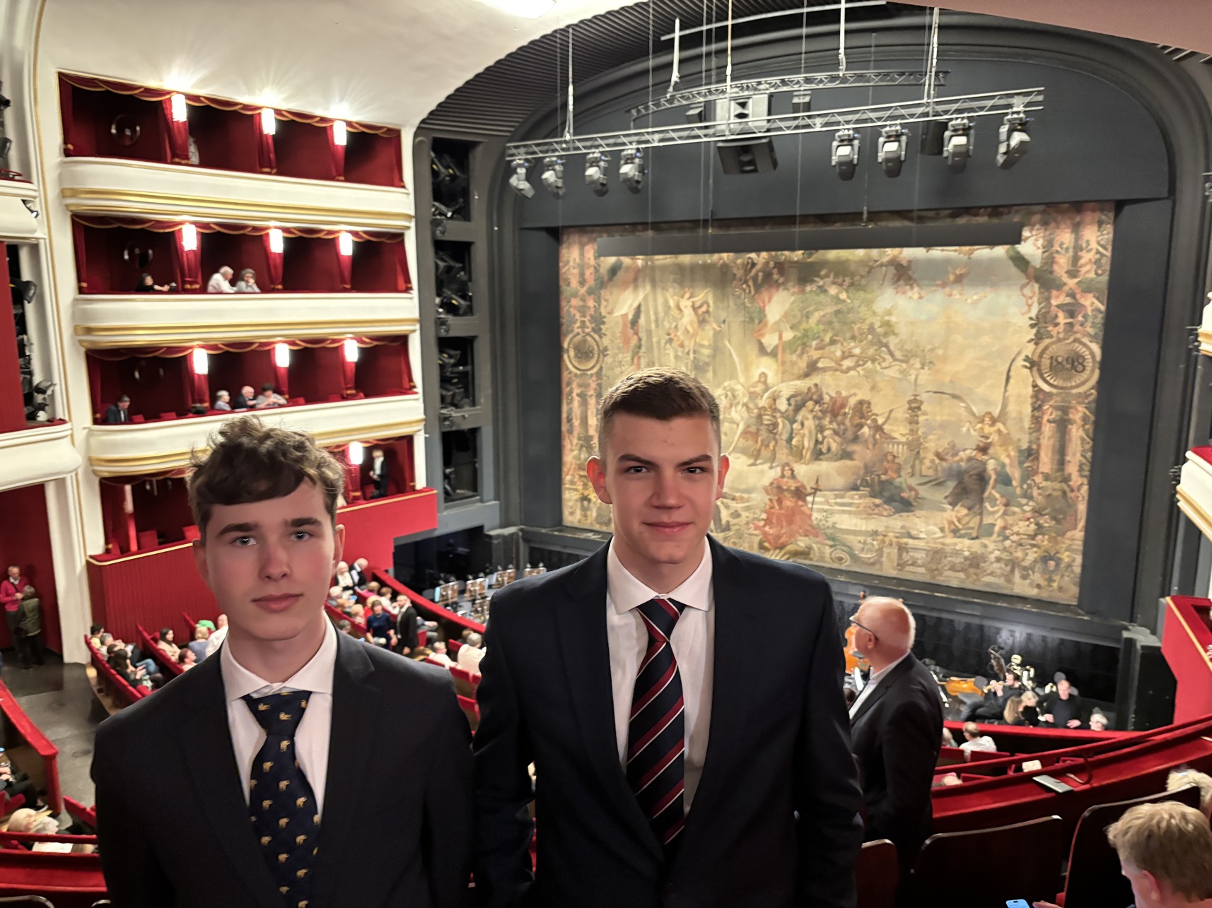 Zwei Teenager in Anzug und Krawatte in einer Loge in einem Opernhaus stehend.