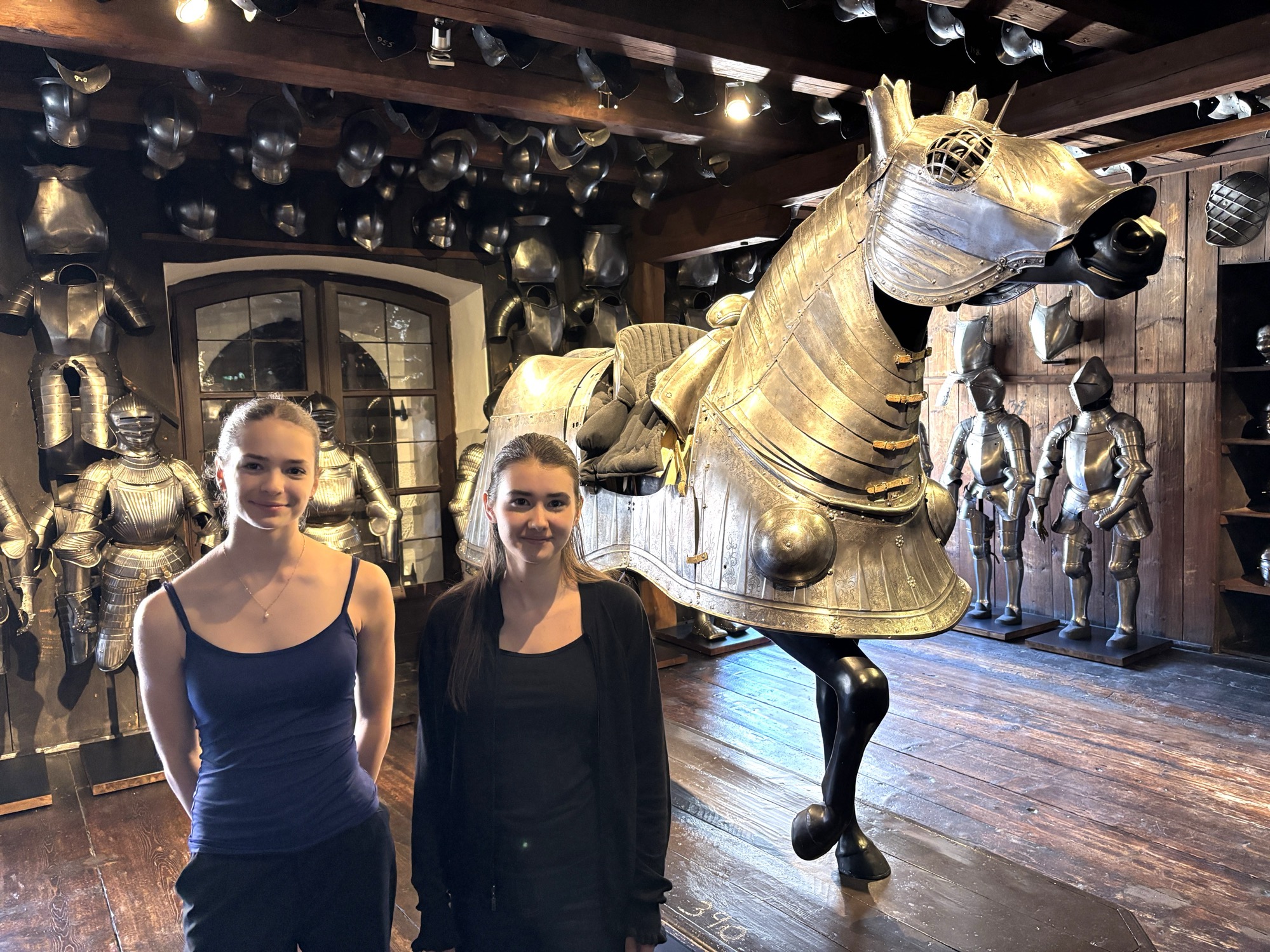 Zwei jung Frauen vor einem Pferd aus Metall posierend mit Rüstungen und weiteren Metallobjekten im Hintergrund.
