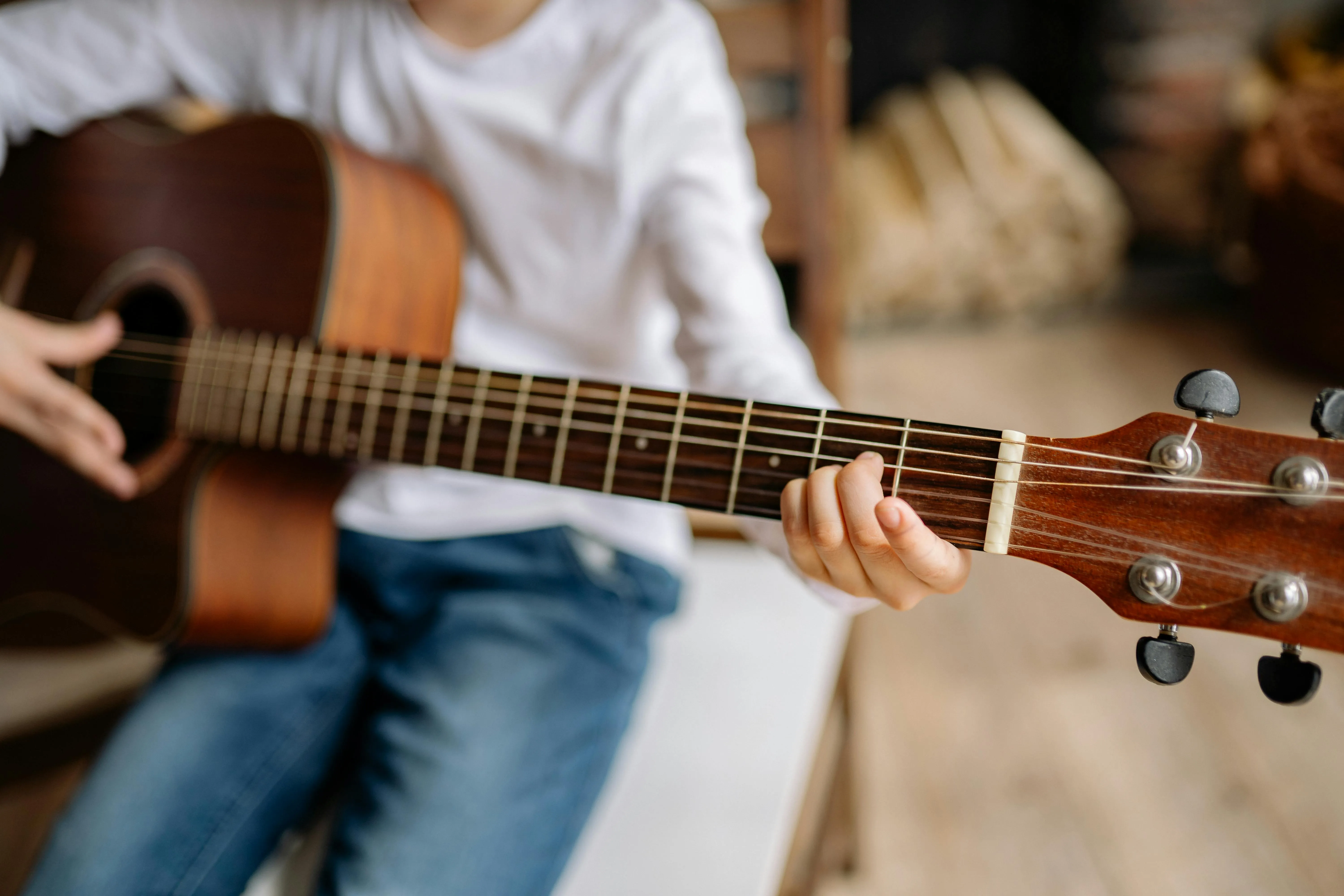 Braune Gitarre von einem Buben in Jeans und weißem T-Shirt bespielt mit Fokus auf die Gitarrensaiten.