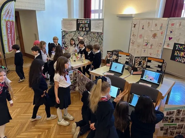 Gruppe von Kindern in Schuluniformen um Tische mit Computern und Stellwänden verteilt