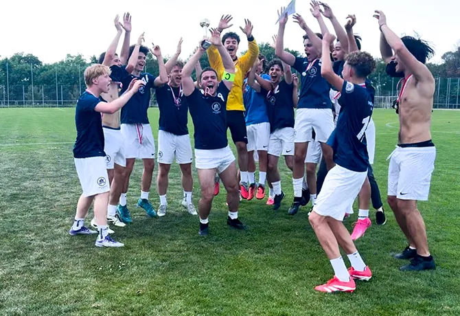 Jubelnde junge Burschen in Fussballdresen mit in die Höhe gerissene Arme.