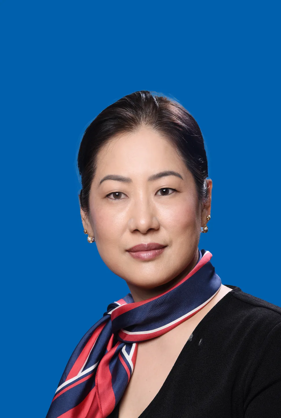 Frau mit dunklem Haar, die goldene Ohrringe und ein blau rotes Halstuch trägt.