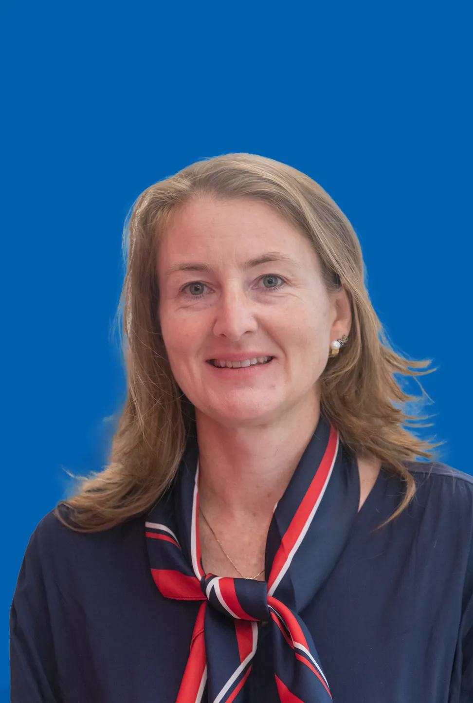 Portraitfoto einer Frau mit hellen langen Haaren, Perlenstecker, blauer Bluse und blau weiß rotem Seidenhalstuch