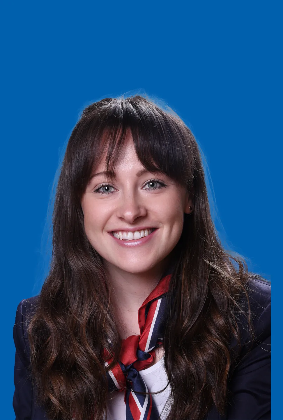 Lächelnde junge Frau mit langen dunklen Haaren, die ein rot-blaues Halstuch trägt.