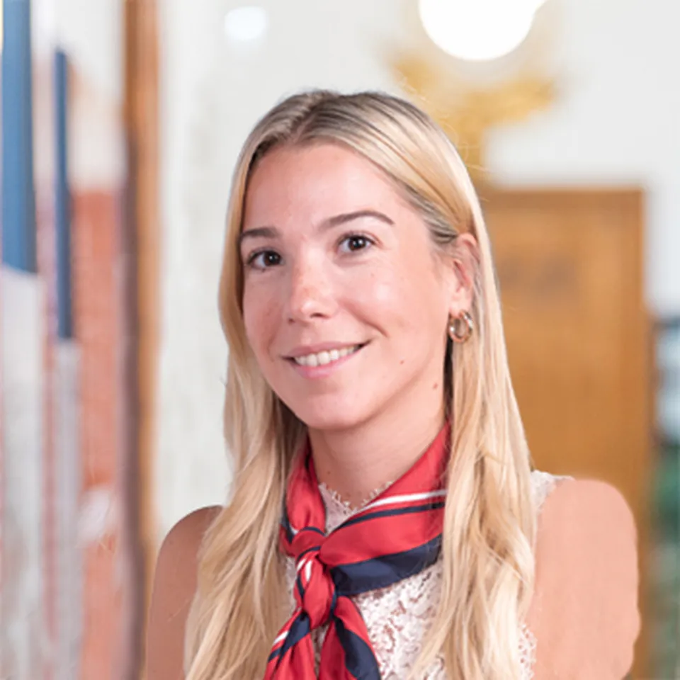 Eine junge Frau mit langen blonden Haaren und einem rot‑blauen Halstuch, die einen freundlichen Gesichtsausdruck hat.