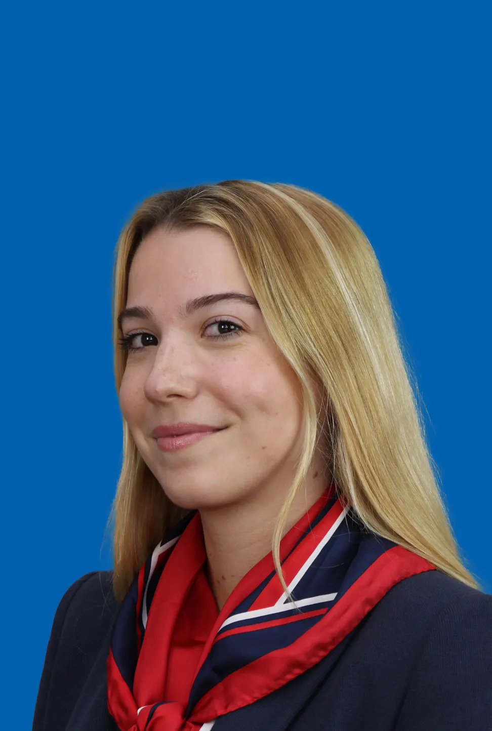 Eine junge Frau mit langen blonden Haaren und einem rot‑blauen Halstuch, die einen freundlichen Gesichtsausdruck hat.