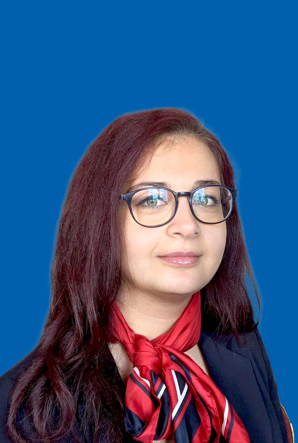 Eine junge Frau mit dunkelrotem, langem Haar, Brille und einem rot‑blauen Halstuch, die einen freundlichen Ausdruck zeigt.