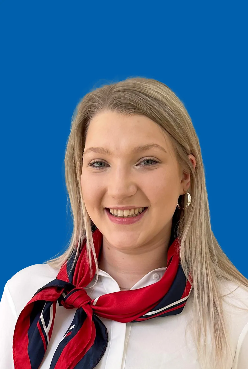 Eine junge Frau mit langem blondem Haar, die Ohrringe und ein rot blaues Halstuch trägt und freundlich lächelt.