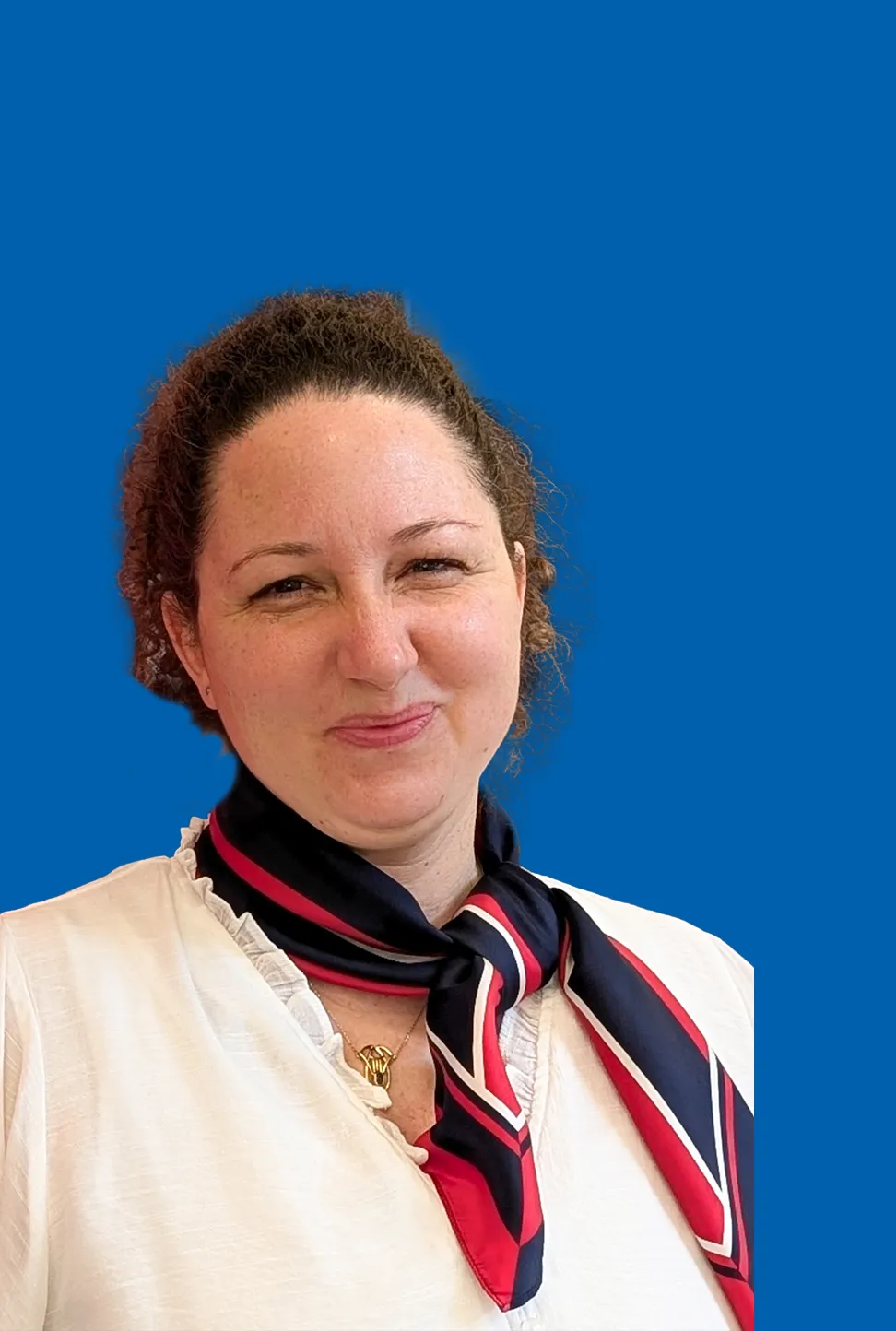 Frau mit dunklen Haaren, die eine weiße Bluse und ein rot-blaues Halstuch trägt.