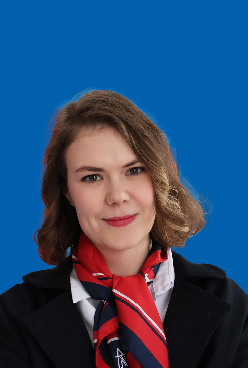 Eine junge Frau mit kurzem brünetten Haar, die ein rot blaues Halstuch trägt und freundlich lächelt.