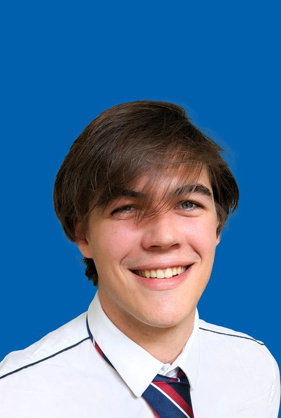 Junger Mann mit braunem Haar, der lächelt und ein weißes Hemd mit einer rot-blau gestreiften Jacke trägt.