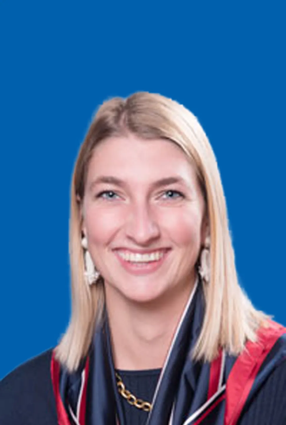 Blonde lächelnde Frau, die Ohrringe, Kette und ein rot-blaues Tuch trägt.