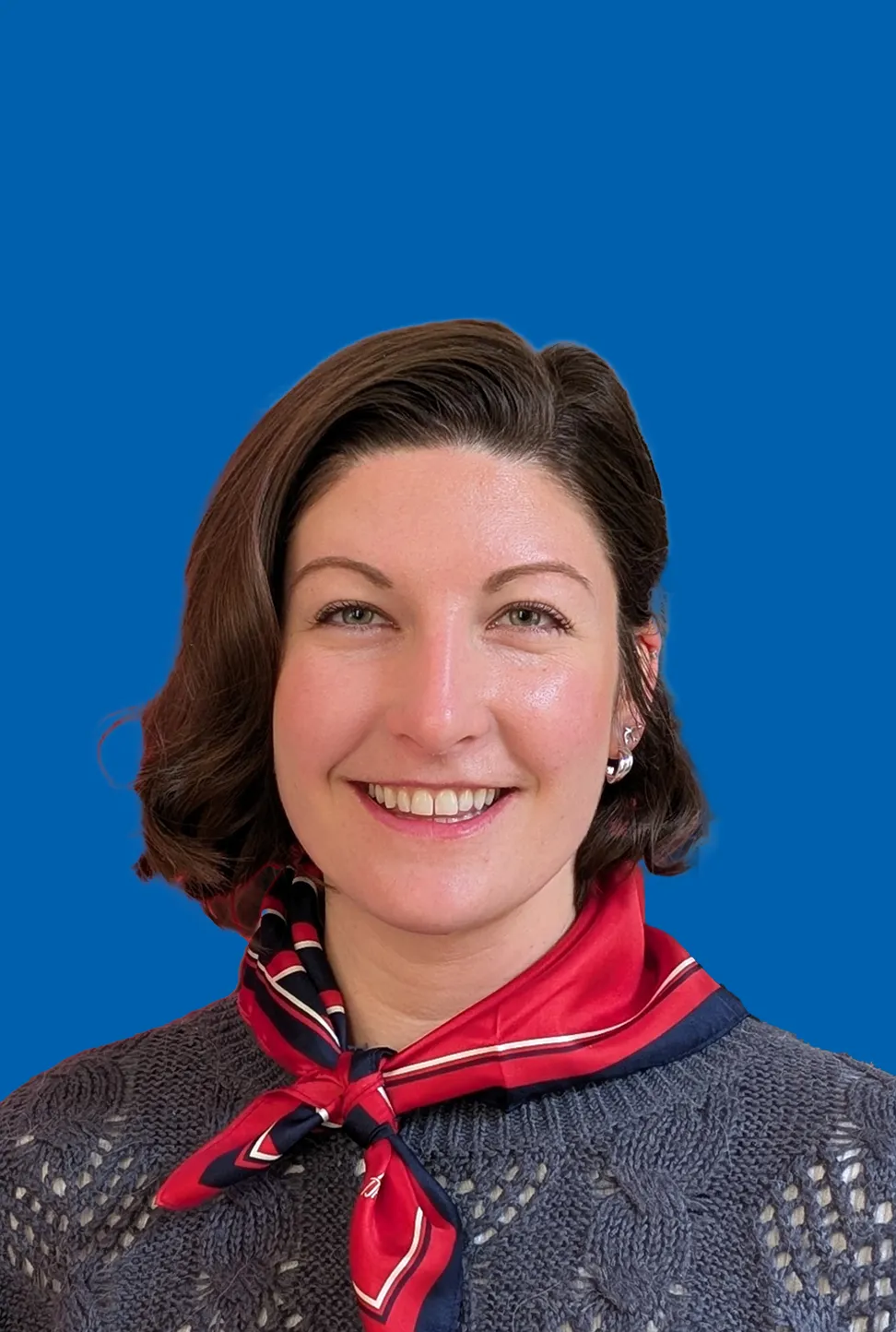 Eine lächelnde Frau mit dunklem kurzen Haar, die Ohrringe und ein blau rotes Halstuch trägt.