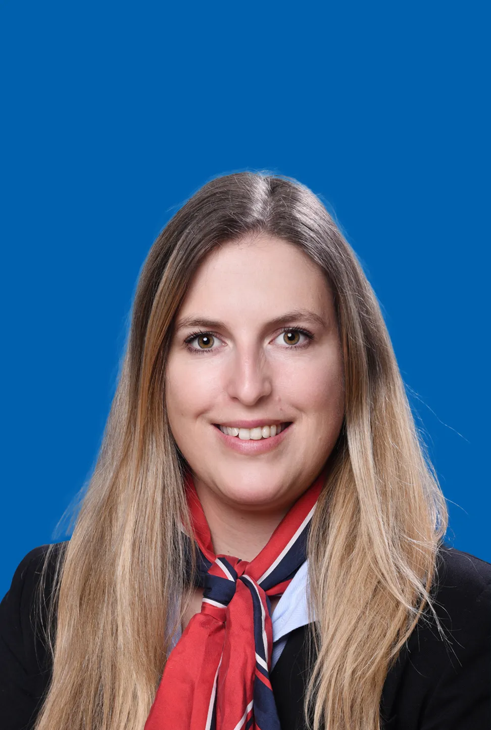 Junge Frau mit langem blonden Haar, die ein rot blaues Halstuch trägt und freundlich lächelt.