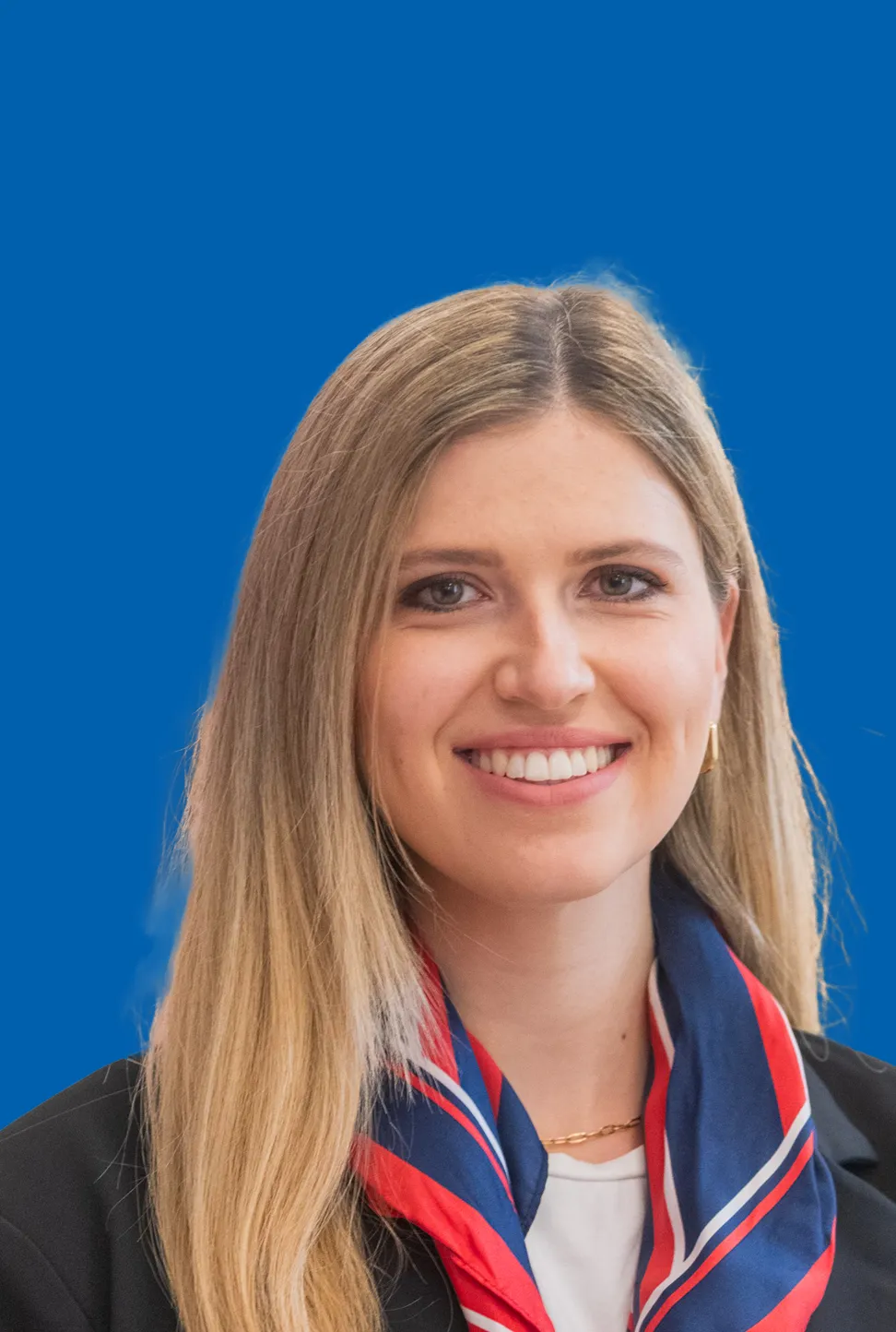 Lächelnde junge Frau mit blondem, langem Haar und einem rot blauen Halstuch.