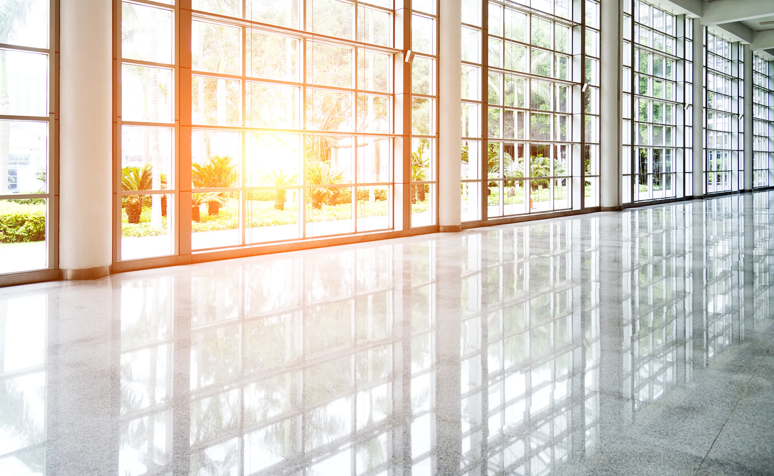 Empty lobby with large windows and white floor. A spacious and bright area with no people, featuring floor-to-ceiling windows and a pristine white floor