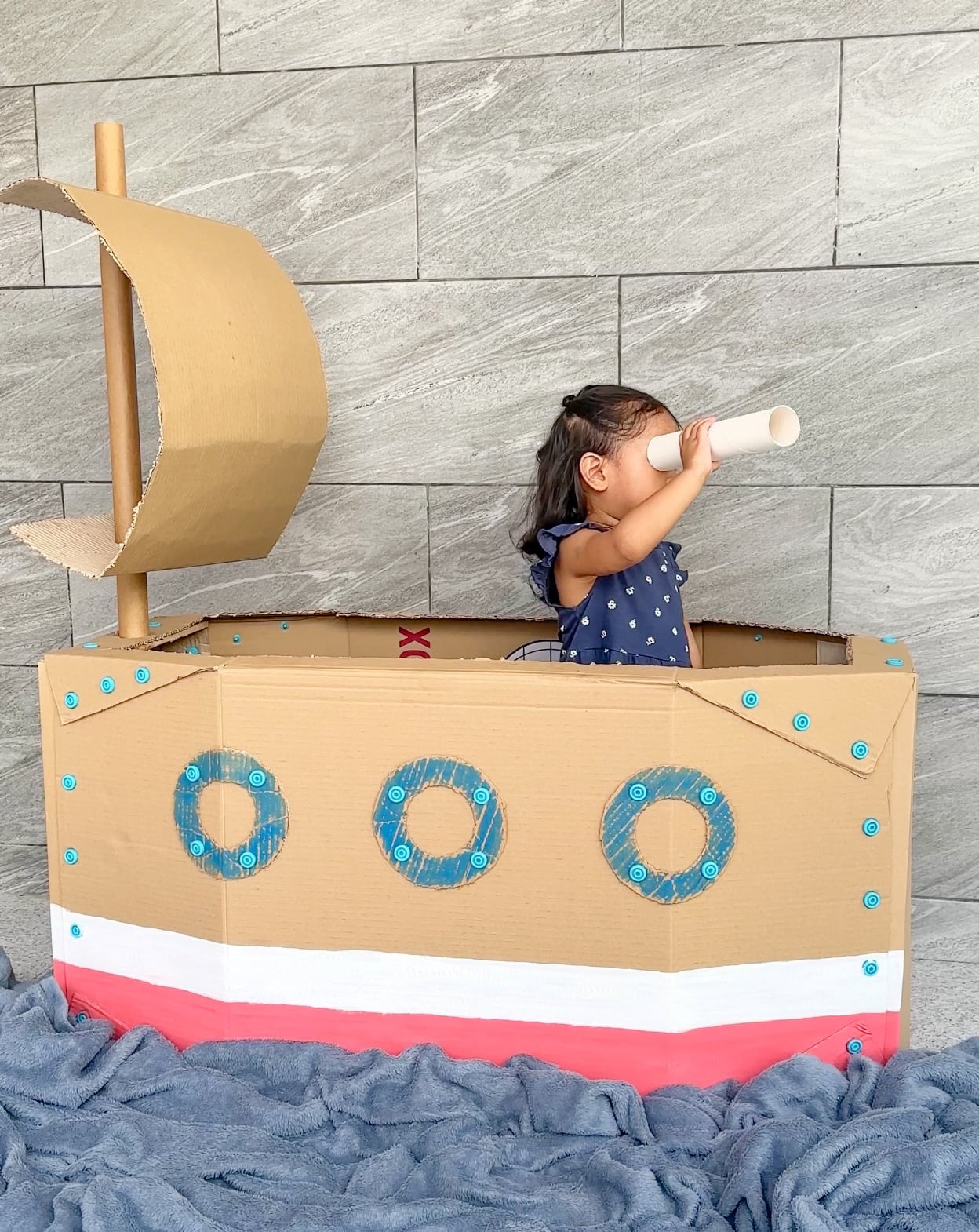 Cardboard Makedo sailing boat with a girl looking through a paper tube telescope.