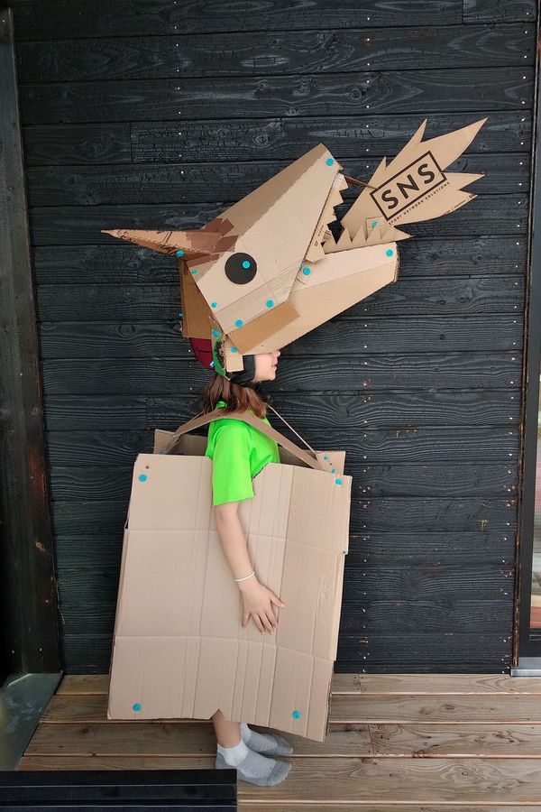 Child wearing a cardboard Makedo dragon costume, testing the fit before the costume is painted.