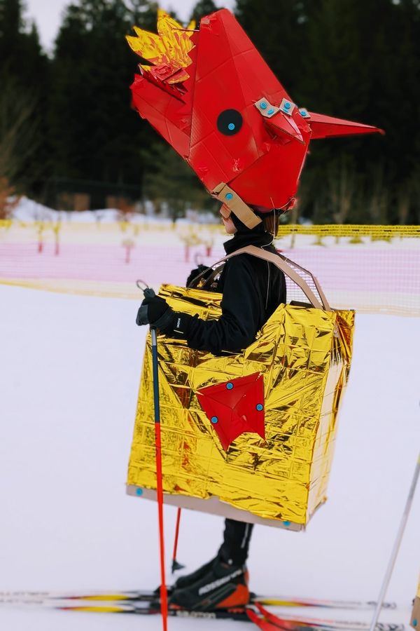 Child skiing while wearing the head section of a group cardboard Makedo dragon costume.