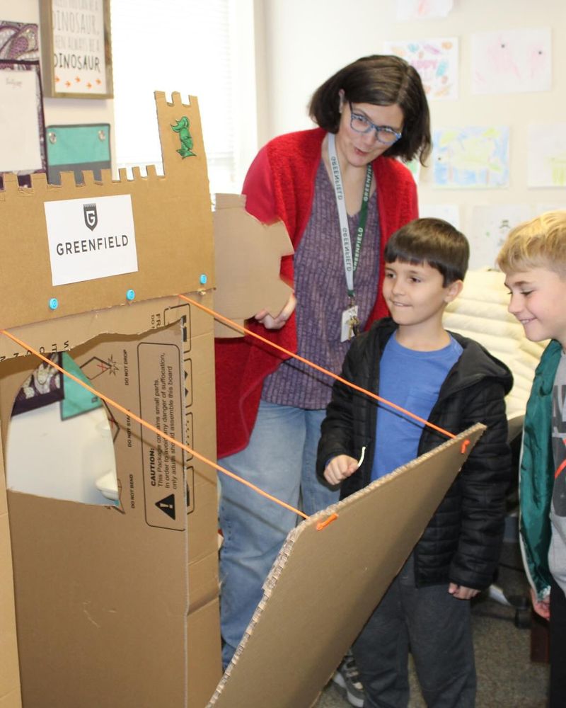 A teacher shows two children how the drawbridge works on a cardboard castle built using Makedo connectors.