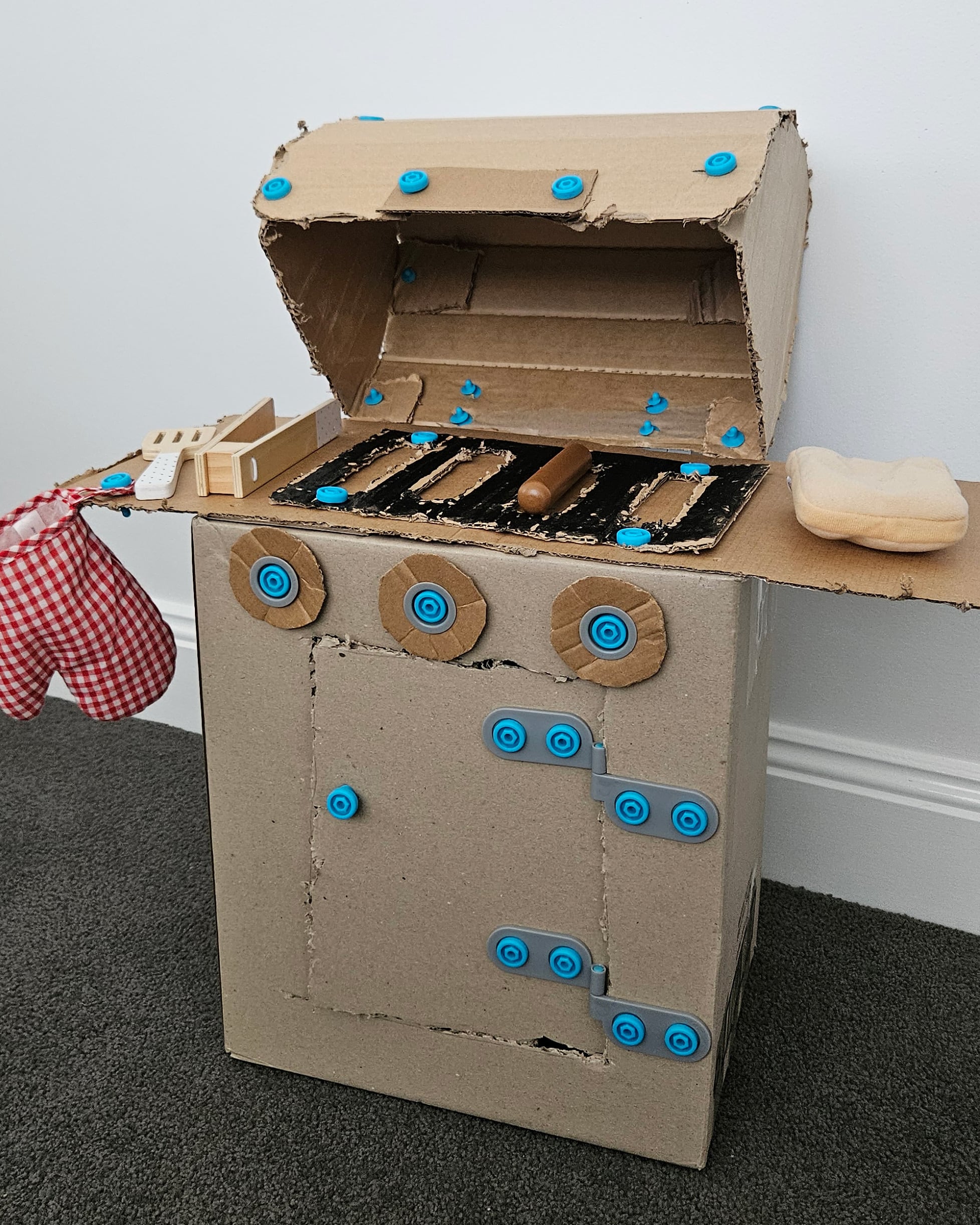 Cardboard Makedo BBQ with open lid, showing a toy sausage on the grill.