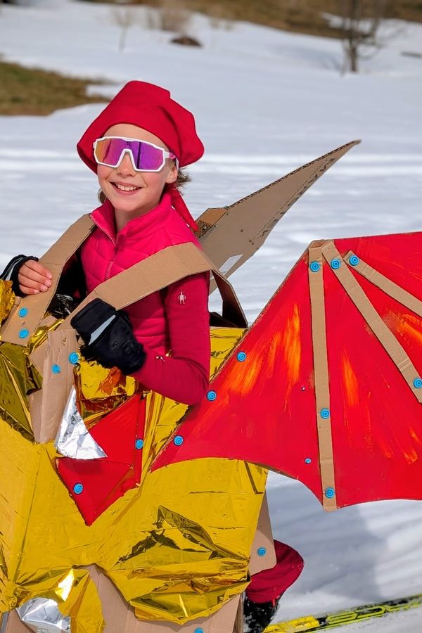 Child skiing while wearing a cardboard Makedo dragon costume, with a big happy smile on her face.