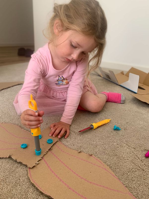 Young girl in a pink dress focuses on assembling cardboard pieces with a Makedo Scru-Driver.