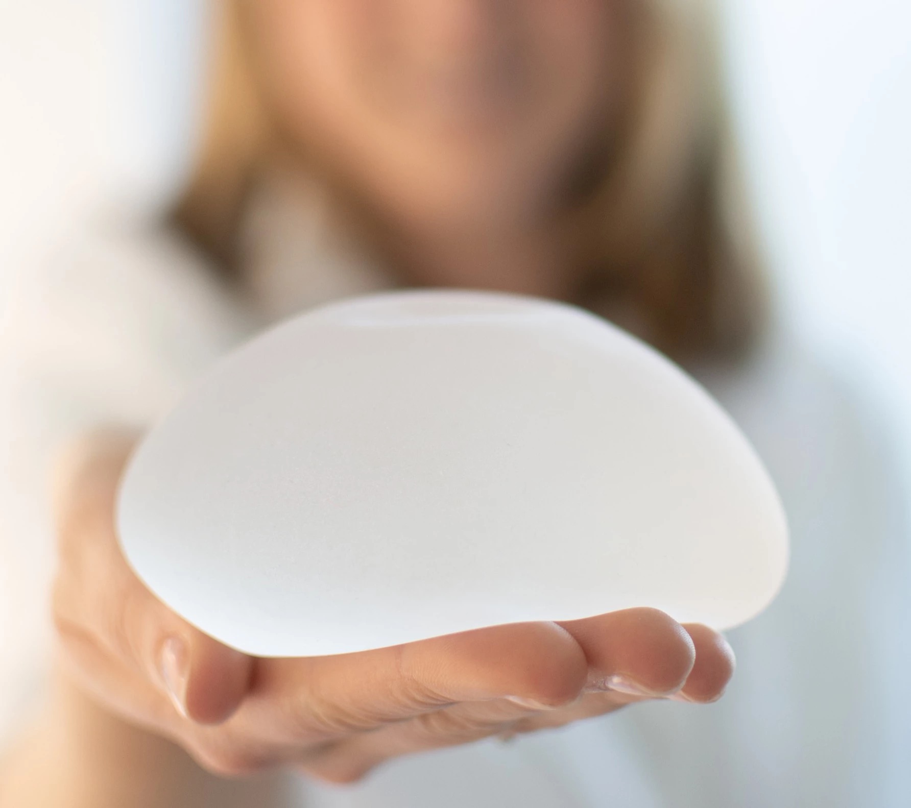 Dr. Jennifer Kager hält ein Brustimplantat in ihrer Hand, im Rahmen einer Darstellung von Brustbehandlungen.