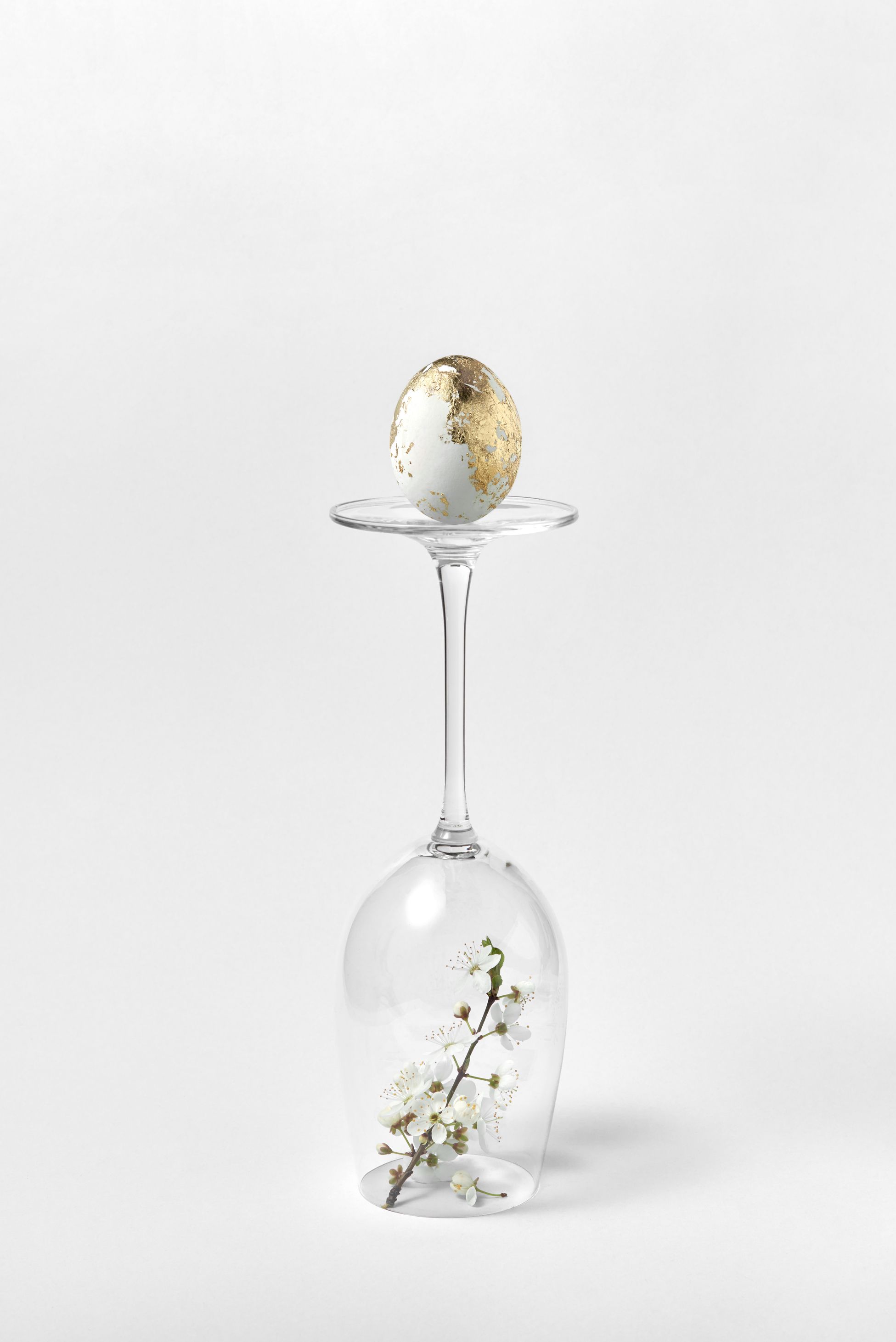 gilded egg resting on wine glass with a cherry blossom underneath